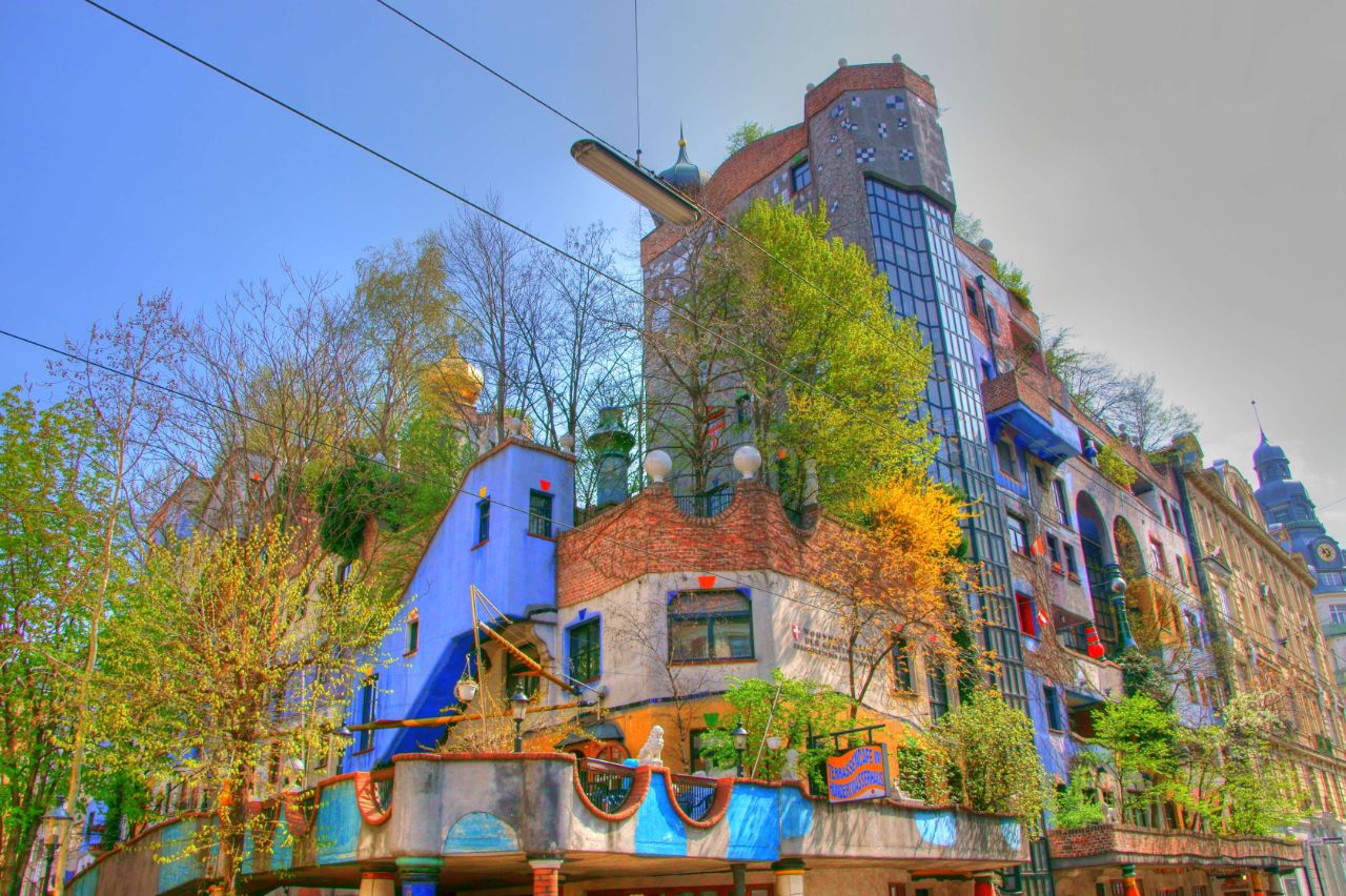 The colorful and unconventional facade of the Hundertwasserhaus in Vienna with irregular shapes and a tree growing from a window.